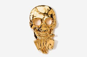 A gold skull with four cards and a cigarette.