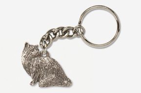 A silver key chain with a cat sitting on the ground.